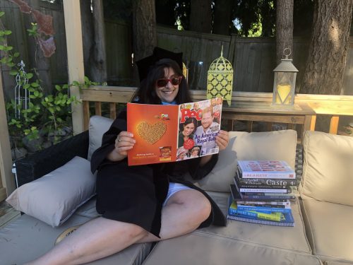 sitting by a stack of books while reading a magazine